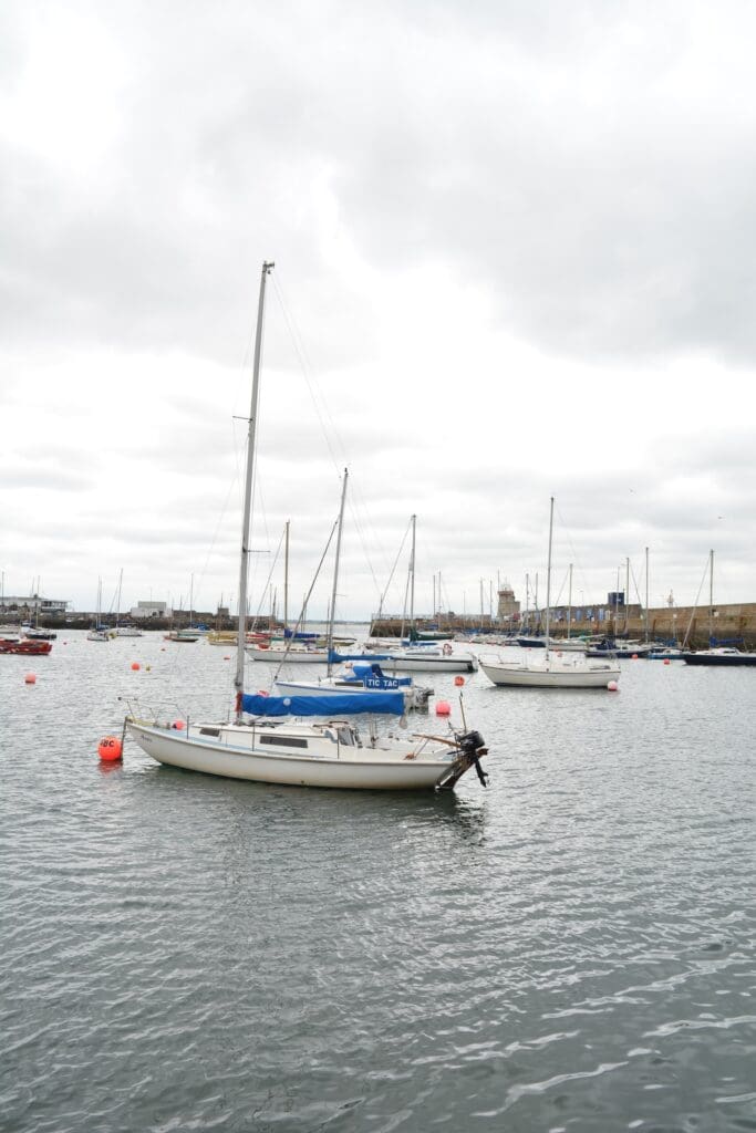 Sailboat with lowered blue sail in harbor in Howth, Ireland.