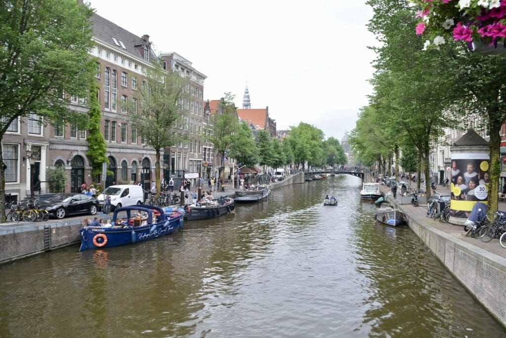 Amstel River in Amsterdam on an overcast day. Boats line river edges and bikes line street edges.