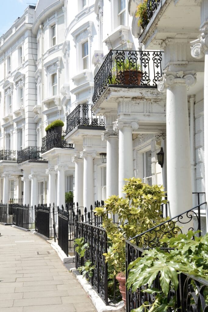 White row homes in London with ornate white pillars and black iron fencing.