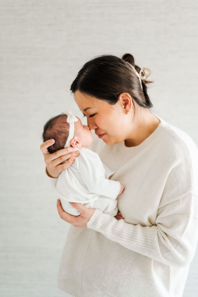 Mother holds her newborn baby up to nuzzle their noses together.