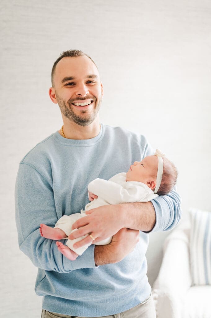 New dad holds newborn baby with white onesie and bow.
