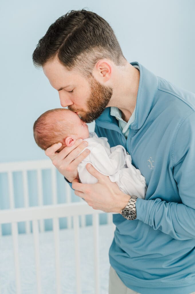 New dad holds newborn baby up as he kisses his forehead.